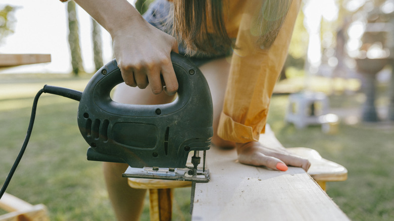 Woman cutting wood with a jigsaw in a backyard