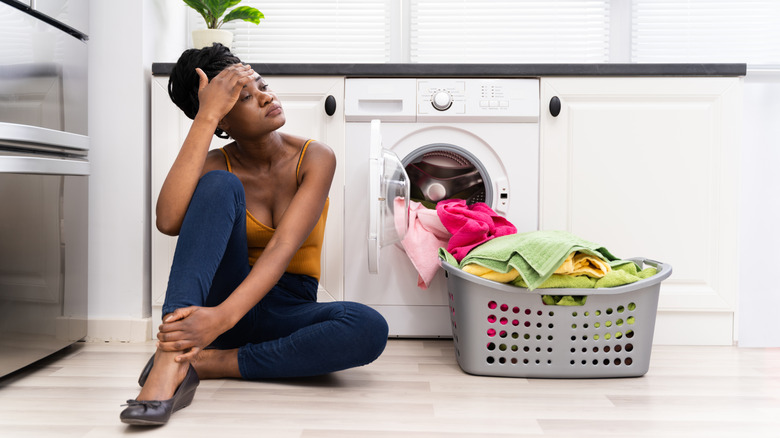 A woman sits by her dryer, looking tired