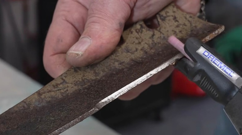 Person sharpening lawn mower blade with Dremel rotary grinder