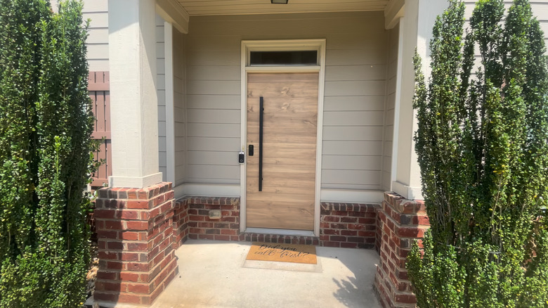 A contemporary front door is flanked by two tall green trees
