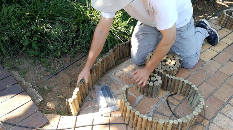 Person installing a rolled log edging material along a garden bed