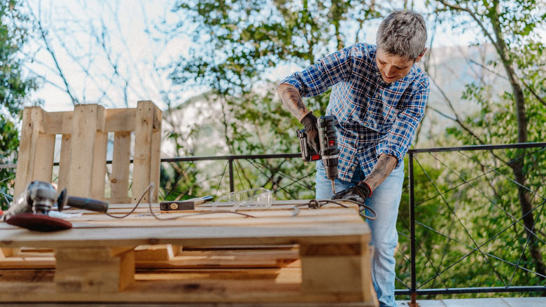 Older woman drilling into a wood pallet