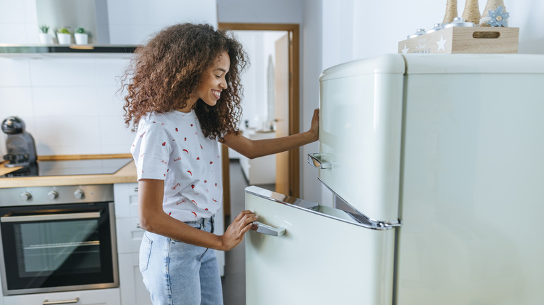 Woman opening vintage-looking fridge in clean kitchen