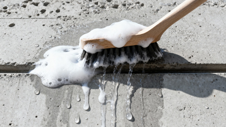 Close-up of a wood handled brush scrubbing gray concrete