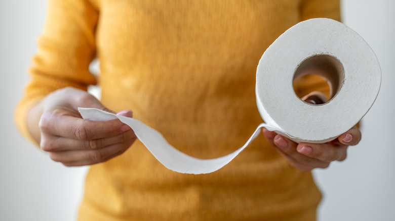 A person wearing a yellow sweater holding roll of unraveling toilet paper