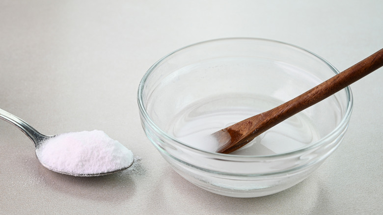 A bowl of water beside baking soda on a spoon