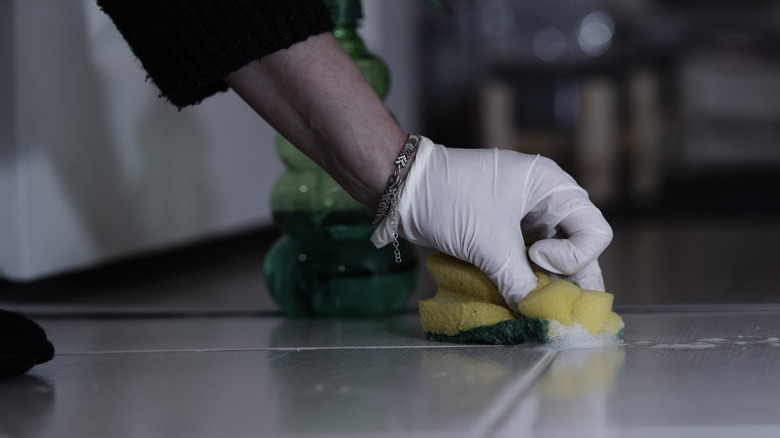 Hand scrubbing floor grout with sponge and a cleaning agent