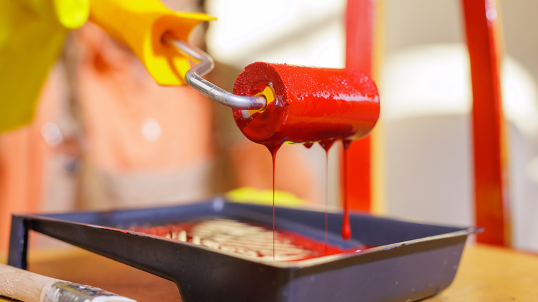 Paint roller covered in red paint in tray