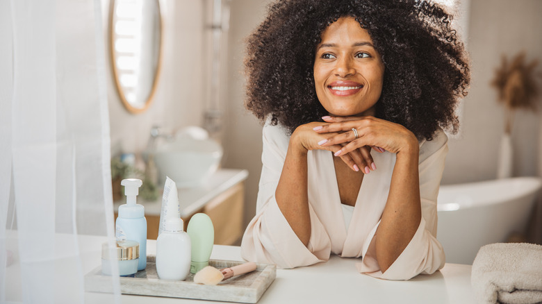 A woman leans over her bathroom counter with a vintage tray holding cosmetic items.