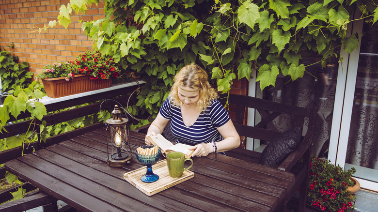 Woman sitting at a table on a balcony covered with vines