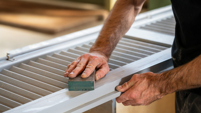 A person sanding on wooden shutter