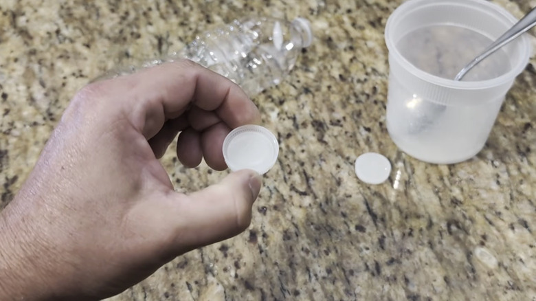A person holding a bottle cap ready to fill it with DIY ant bait.