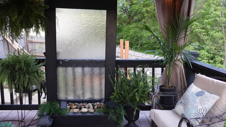 A tall shower door water wall sits on a patio surrounded by ferns