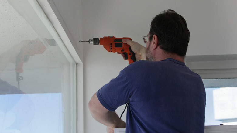 A person drilling into wall above a window