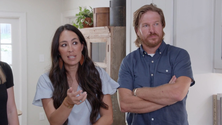 Joanna Gaines in a white kitchen with a hesitant look on her face, standing next to Chip Gaines