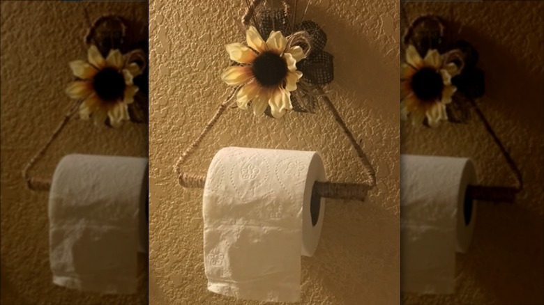rustic toilet paper holder made from wire hanger, twine, and faux greenery