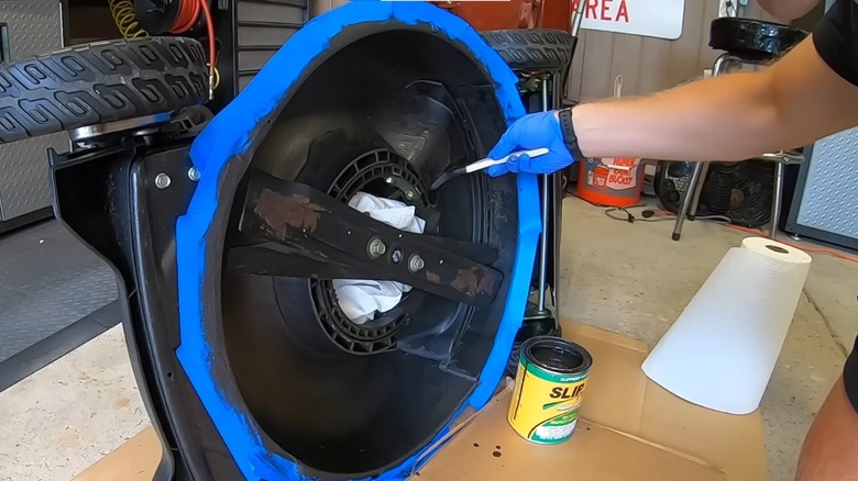 person applying Slip Plat dry lubricant on lawn mower deck