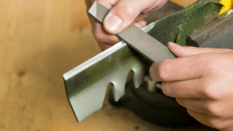 a person using a file to sharpen a lawnmower blade