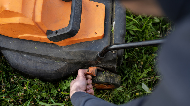 a person adjusting wheel height lever on electric lawn mower