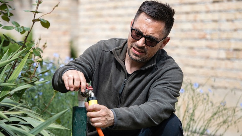 Man struggling to disconnect stuck hose from outdoor spigot