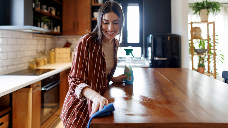 Woman cleaning a reddish-brown wood island countertop surface