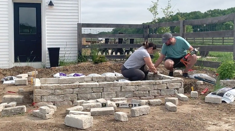 Couple building a rustic limestone raised garden bed.