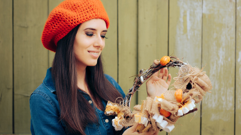 A woman in an orange hat smiles and holds a Halloween themed wreath