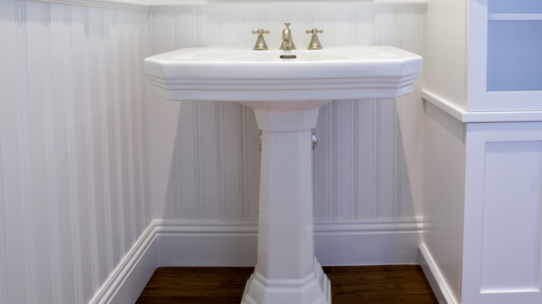 white pedestal sink with gold hardware in white and green bathroom