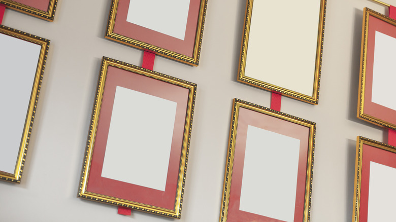 gold frames hung vertically on a wall and connected by red ribbons