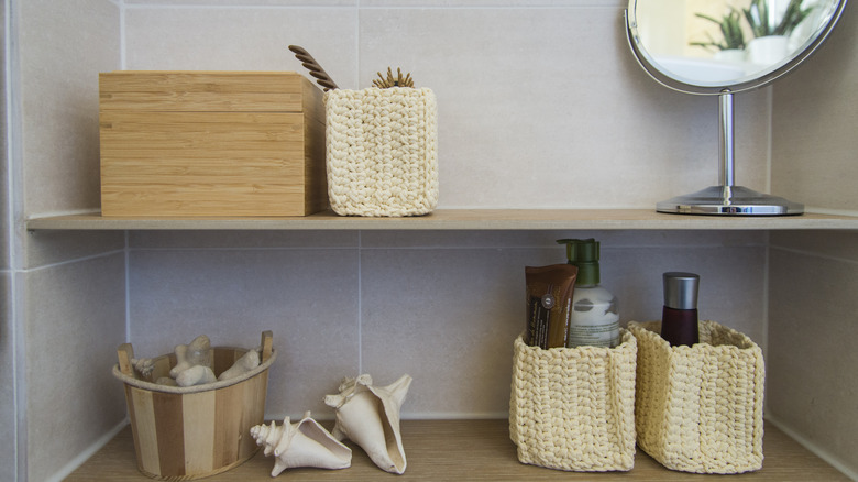 tan tiled wall with wooden shelves and holding a mirror, shells, and skincare products