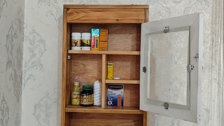 medicine closet with wooden shelving in bathroom with wallpaper