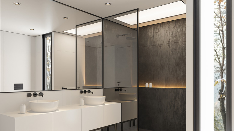 bathroom with large mirrored wall, two sinks, and a shower with a skylight