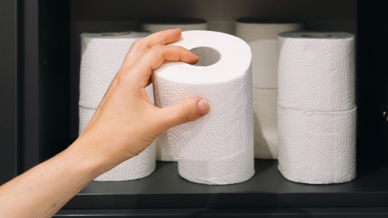 Hand taking toilet paper roll off of an open bathroom shelf