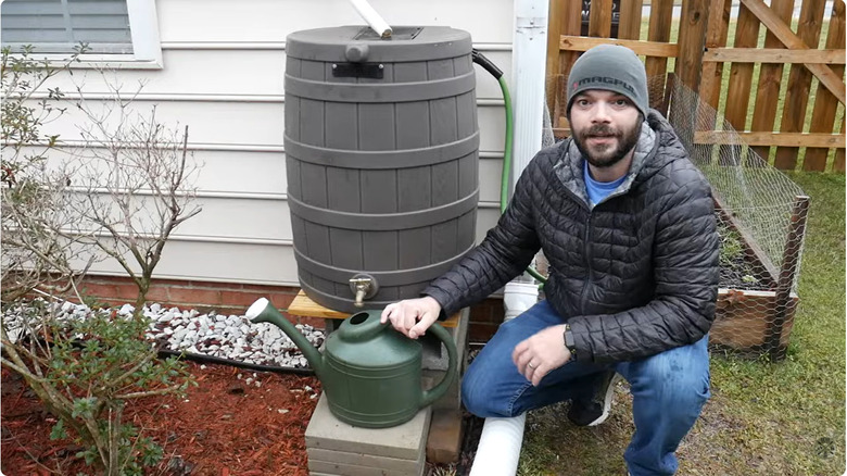 A man stands next to a rain barrel on a homemade, level base made from concrete blocks.
