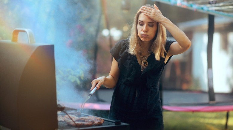 Overwhelmed woman visibly struggling with cooking on backyard grill