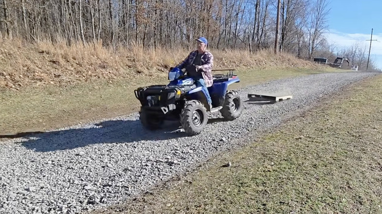 Older homeowner on ATV leveling his gravel driveway with a pallet