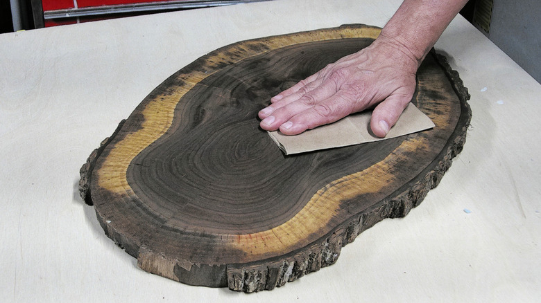A hand smoothing a wood finish with brown paper bag paper