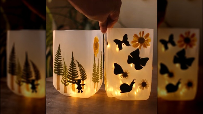 DIY lanterns made from milk jugs with nature shapes on them and lights inside