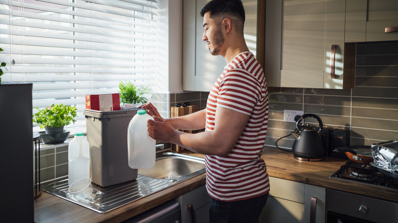 Man holding an empty milk jug next to the recycling container on the kitchen counter