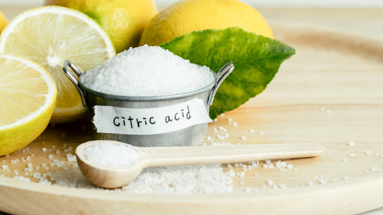 Citric acid crystals in small pot next to fresh cut lemons