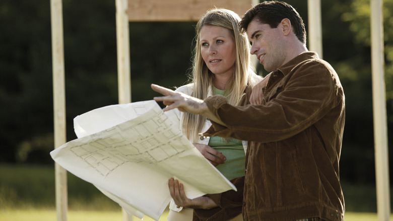 A young couple looks at a site plan while standing near a newly framed house.