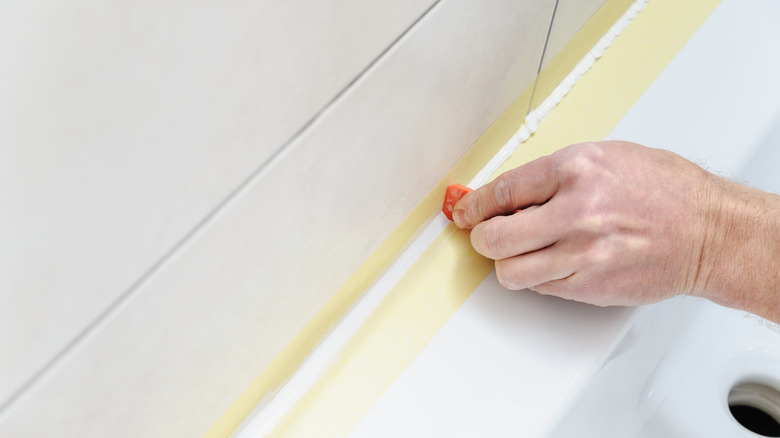 person smoothing caulk with spatula and painter's tape