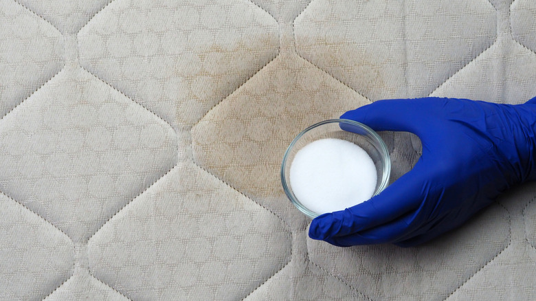 Gloved hand with jar of baking soda on top of a mattress