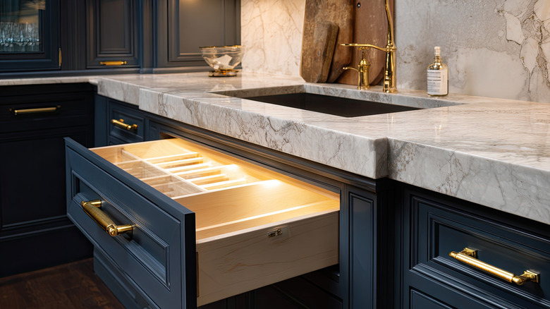 Navy kitchen cabinets are contrasted against thick marble countertops and metallic hardware