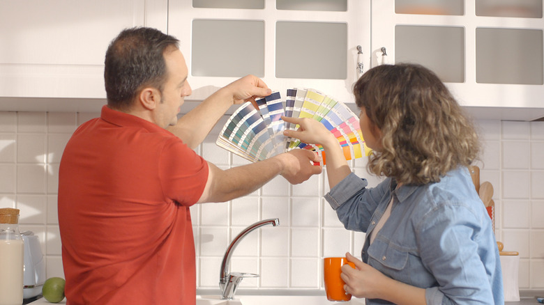A middle-aged couple looks at paint color swatches in a white kitchen