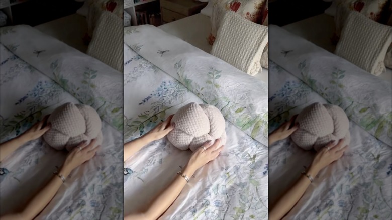 A knotted blanket as a throw pillow on a bed with a floral comforter and other throw pillows