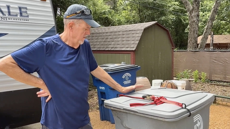 Man observing ratchet strap lock for trash bin