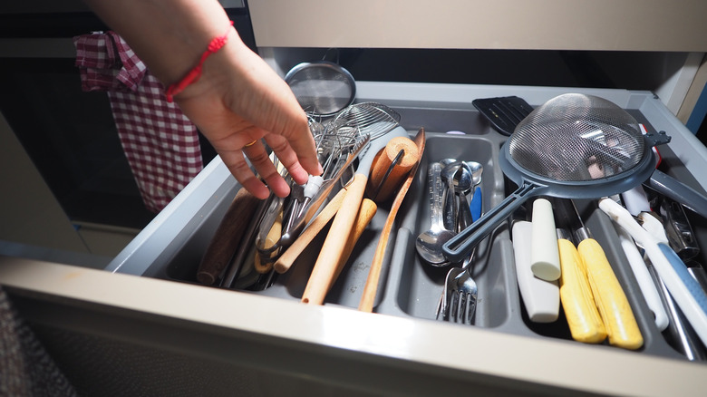 Person reaching into a stuffed kitchen utensil drawer