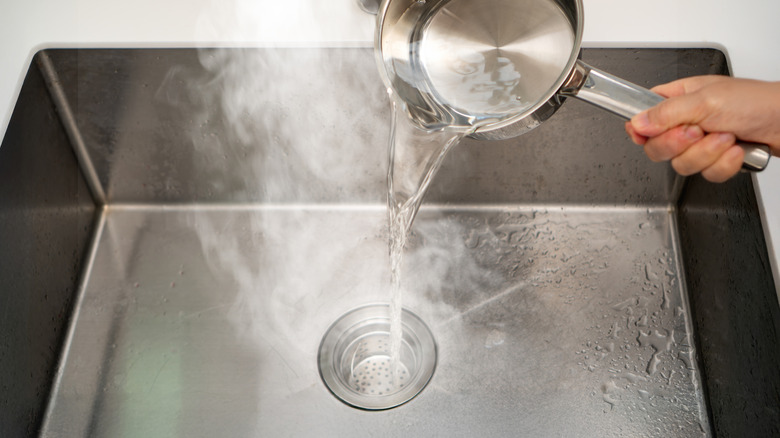 Hand pouring a pot of hot water down the sink