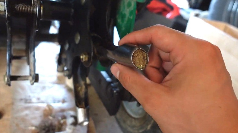 Person checking clogged tine in gas-powered lawn aerator